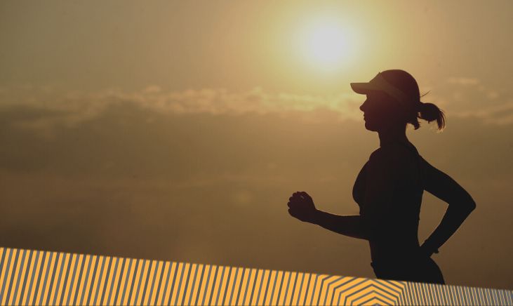 A black silhouette of a woman trail running during a sunset