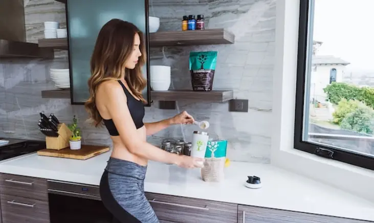 A woman in her kitchen preparing a drink with amino acid's after her workout