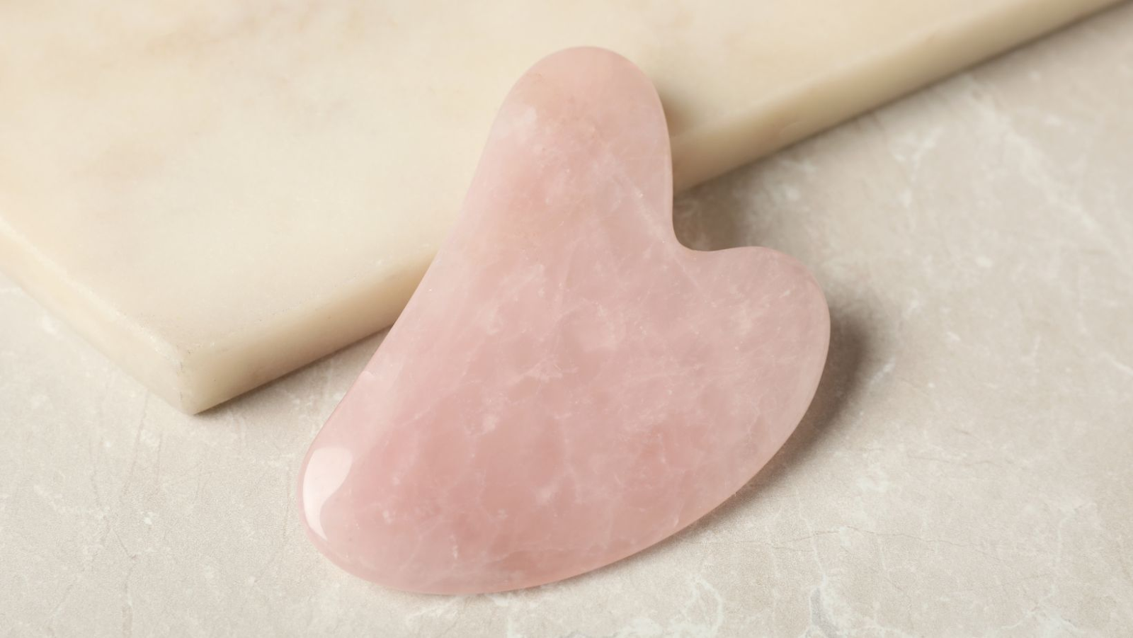 A pink quartz gua sha tool resting on a light coloured surface