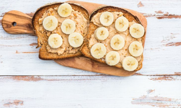 Two piece of toast with slices of banana on them, resting on a wooden cutting board