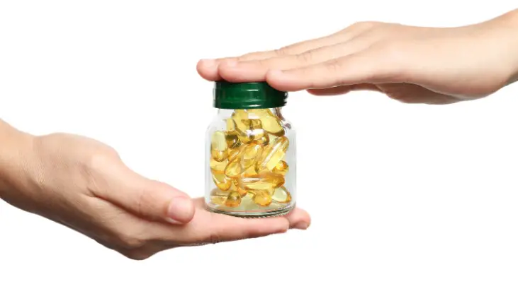 Hand holding fish oil bottle with capsule.


