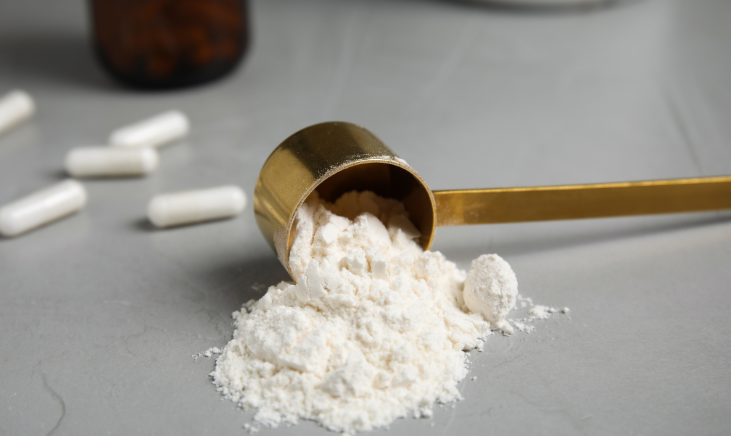 A powder scoop on a surface with a pile of white amino acid powder and some capsules. 
