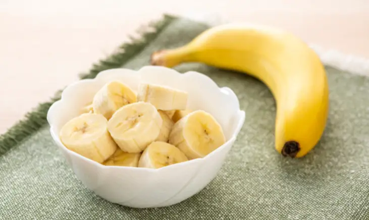 A bowl of sliced bananas with one whole banana next to it.