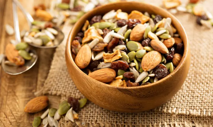 Image of a wooden bowl with a variety of nuts. The nuts include almonds, cashews, beans and peanuts.