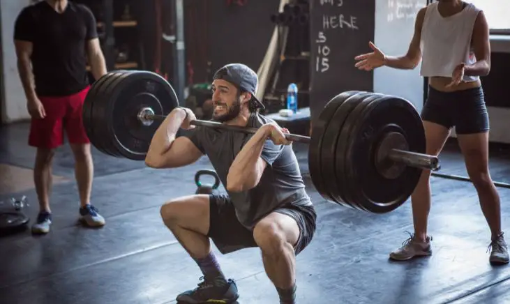 A man doing a heavy front squat lifting weight in a gym in order to build strength and mass