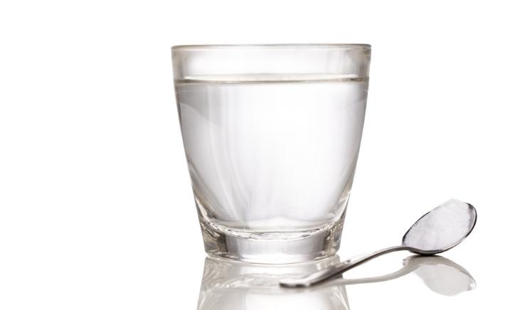 Clear glass filled with water beside a spoon full of salt