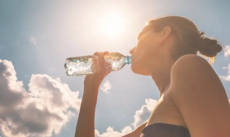 Image of a woman drinking bottled water under the sun.