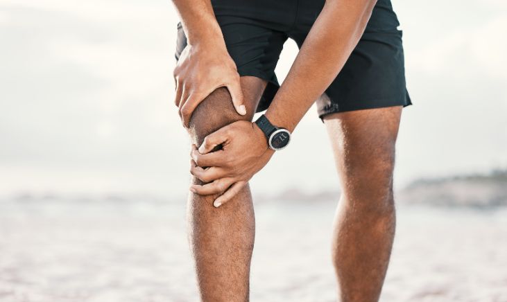 A close-up photograph of a man gently placing his hand on his own knee.