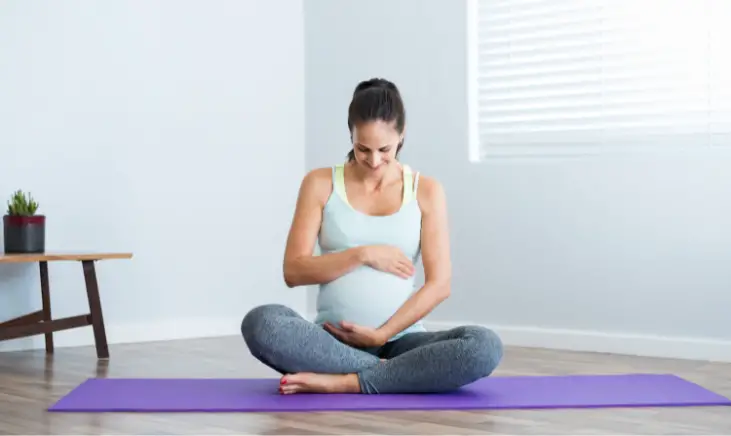 a pregnant woman holding her belly while sitting on a purple yoga mat