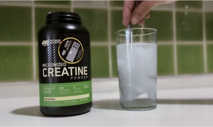 Green Creatine bottle next to a refreshing glass of mixed creatine water