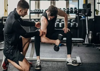 Gym scene with a personal trainer providing support to his student